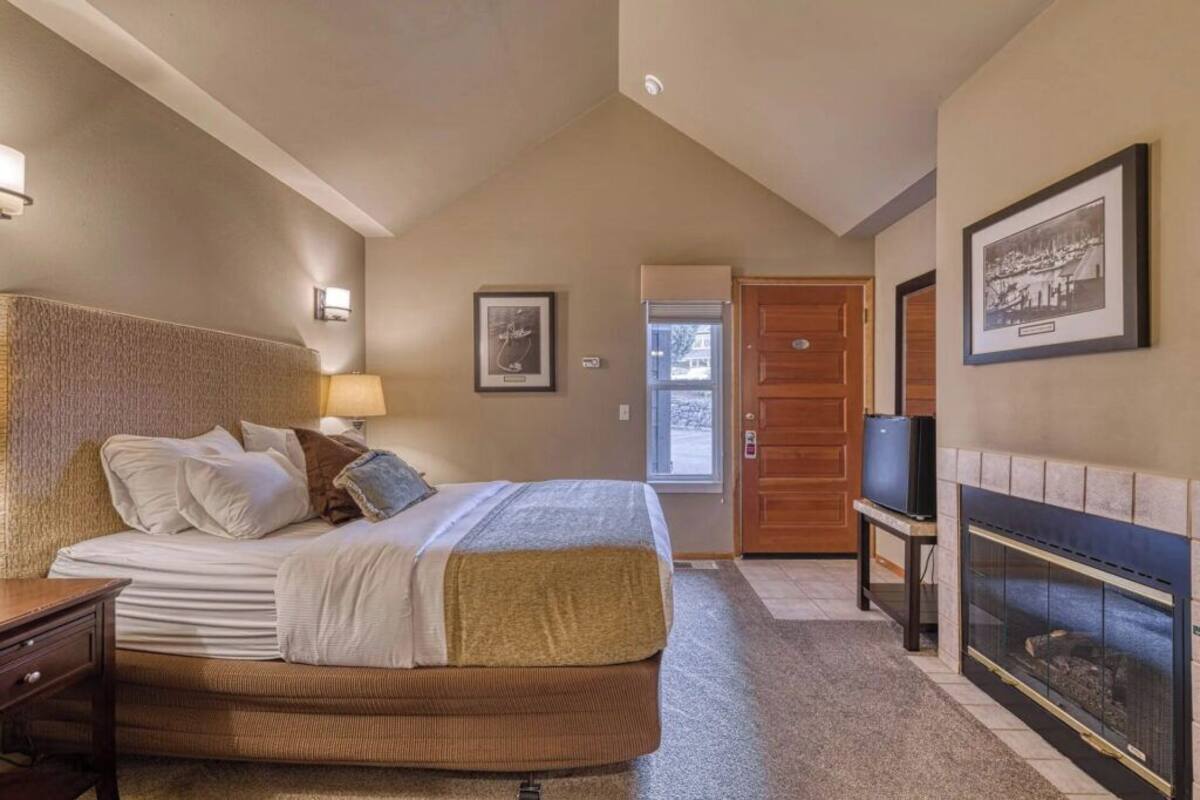 A hotel room with a large bed, a television, a fireplace, and a door leading to another room.