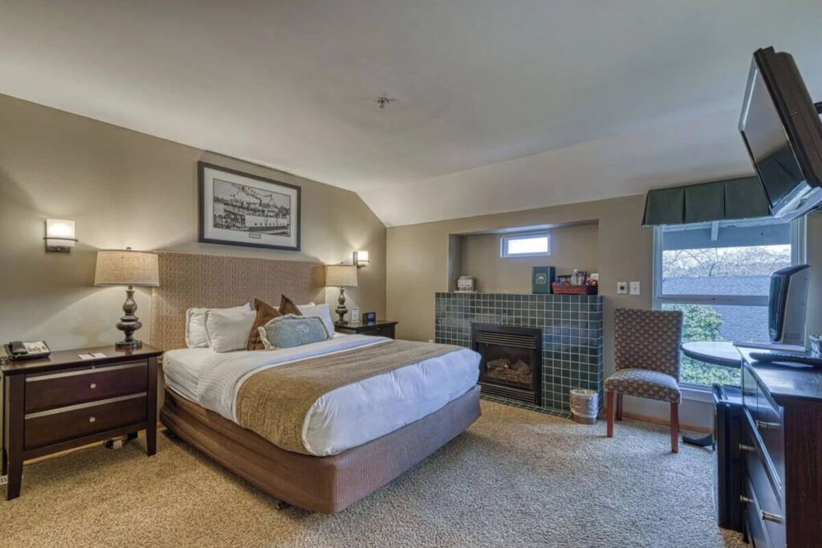 A bedroom with a large bed, a fireplace, a TV, and a desk with a chair.