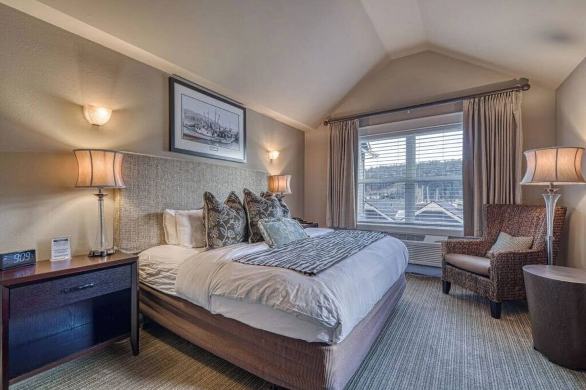 A hotel room with a large bed, two bedside lamps, a chair, a small table, and a window with curtains.