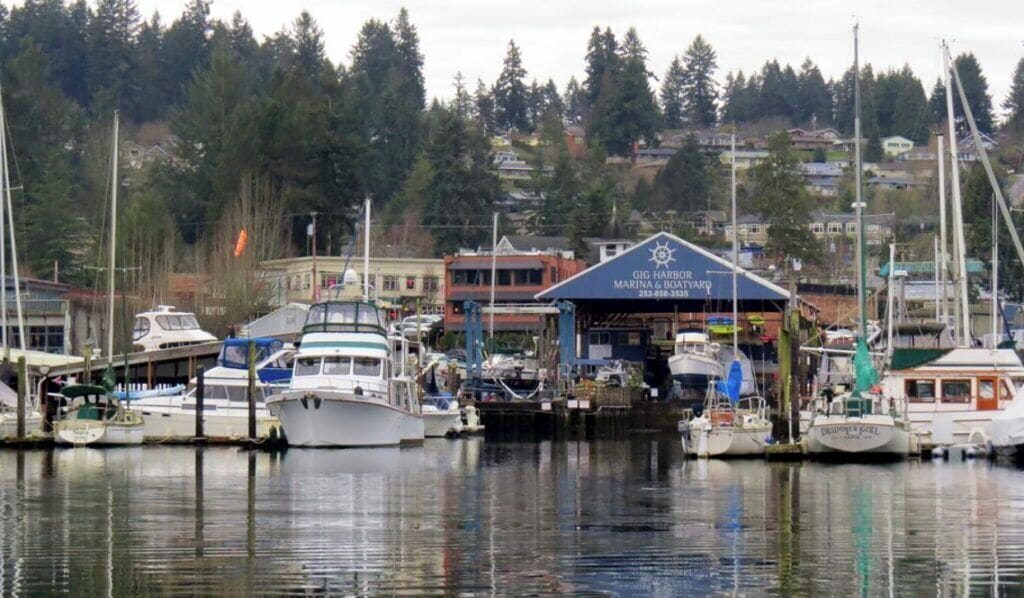 A marina with boats docked, a building labeled 'GIG HARBOUR MARINA & BOATYARD', and a forested hillside in the background.