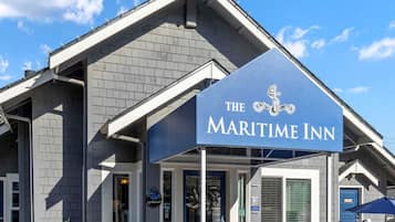 The exterior of The Maritime Inn, featuring a prominent sign with nautical-themed logo, a modern architectural design with grey brickwork, and a clear blue sky in the background.