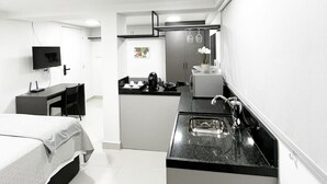Een kleine hotelkamer met een bed, bureau, kitchenette en televisie.