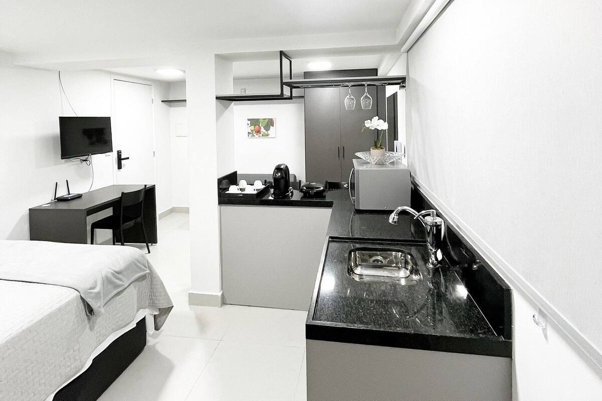 Una habitación de hotel pequeña con cama, escritorio, kitchenette y televisor.
