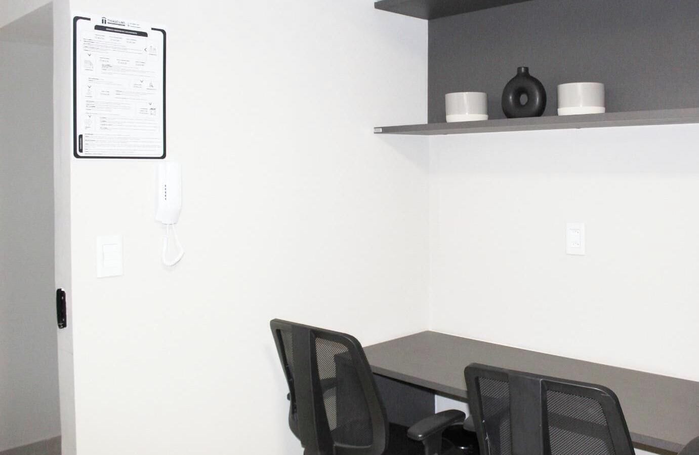 Un salón de conferencias con una pizarra, un teléfono y una estantería con tres tazas blancas.