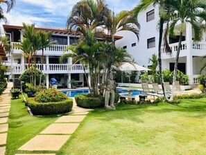 A resort with a swimming pool, palm trees, and a well-maintained lawn. - 3-bedroom condo in perfect Jacó with AC (Jacó)