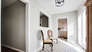 A hallway with a wooden floor, a rug, two chairs, a mirror, and a kitchen in the background. - River Oaks Retreat- Walkable to Goodfellow AFB (San Angelo)