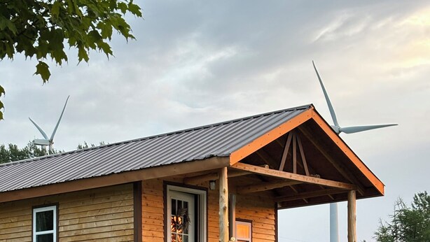 A wooden cabin with a porch, a door, and two wind turbines in the background. - Eastgate cottages on Mars Hill Mountain (Mars Hill)