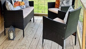 A covered porch with wicker furniture and a view of a grassy field. - Eastgate cottages on Mars Hill Mountain (Mars Hill)