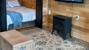 A cozy room with a bed, a television mounted on the wall, and a small black heater. - Eastgate cottages on Mars Hill Mountain (Mars Hill)