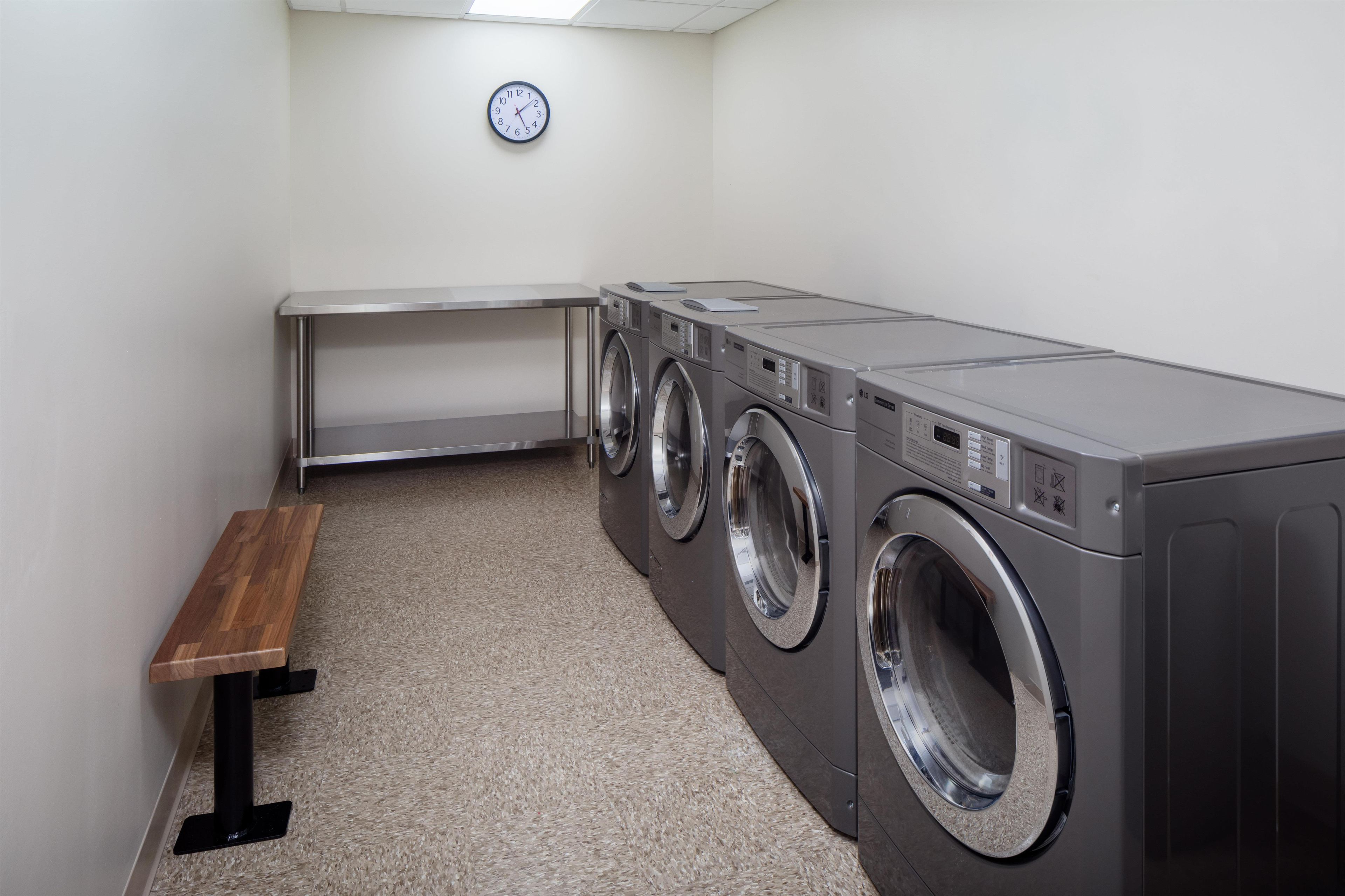 A laundry room with a bench, three stacked washing machines, and a clock on the wall.