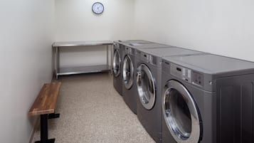 A laundry room with a bench, three stacked washing machines, and a clock on the wall.