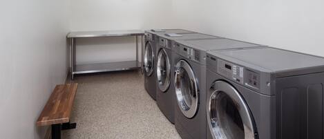 A laundry room with a bench, three stacked washing machines, and a clock on the wall.