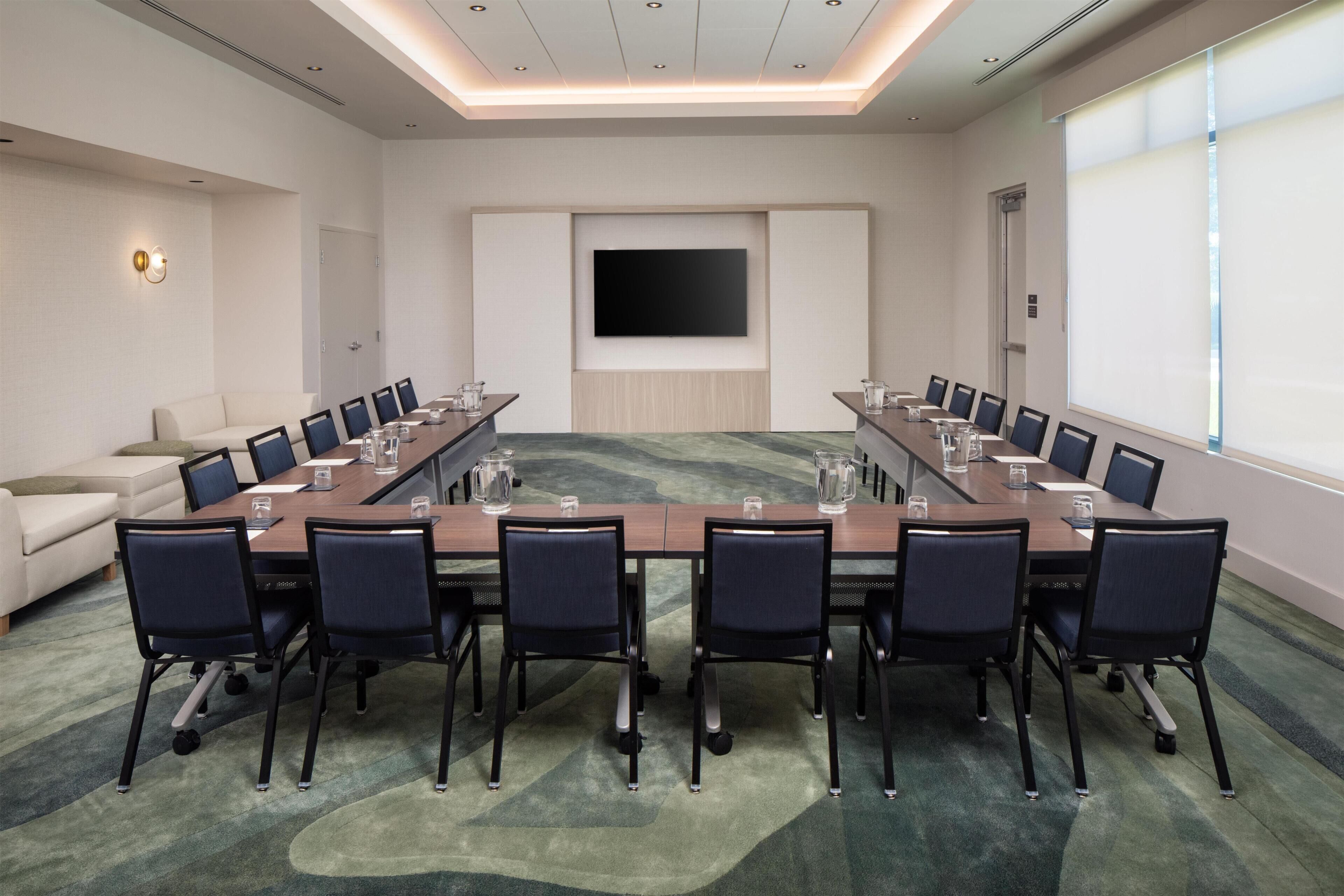 A conference room with a long table, chairs, a television, and a projector screen.