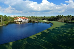 A golf course with a water body, a house with a red roof, and a forested area. - Hyatt House Destin (Destin)