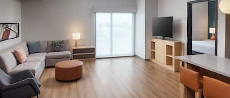 Una sala moderna con sofá, reposapiés, televisor y un comedor con sillas.