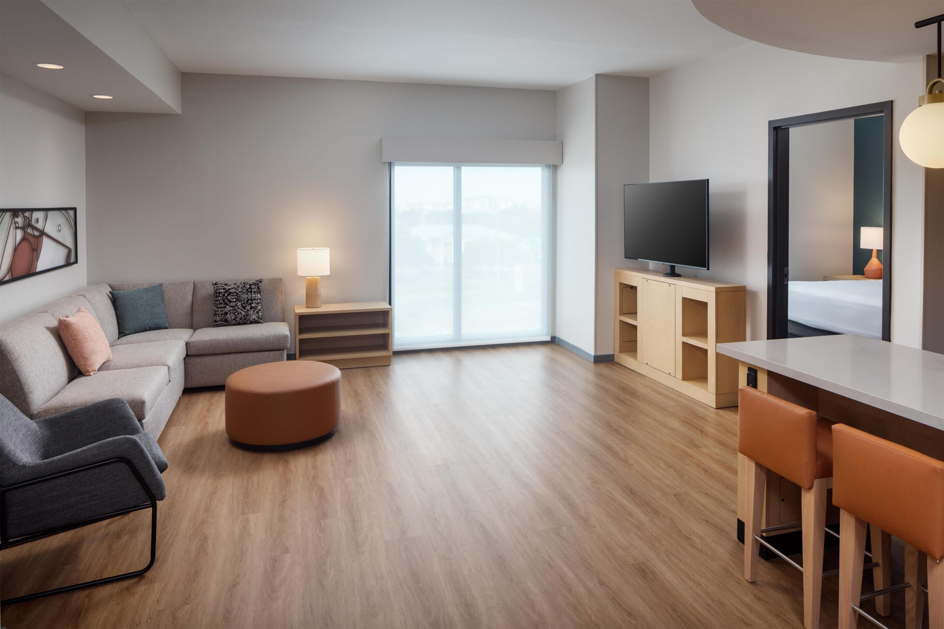 A modern living room with a sofa, ottoman, TV, and a dining area with chairs.