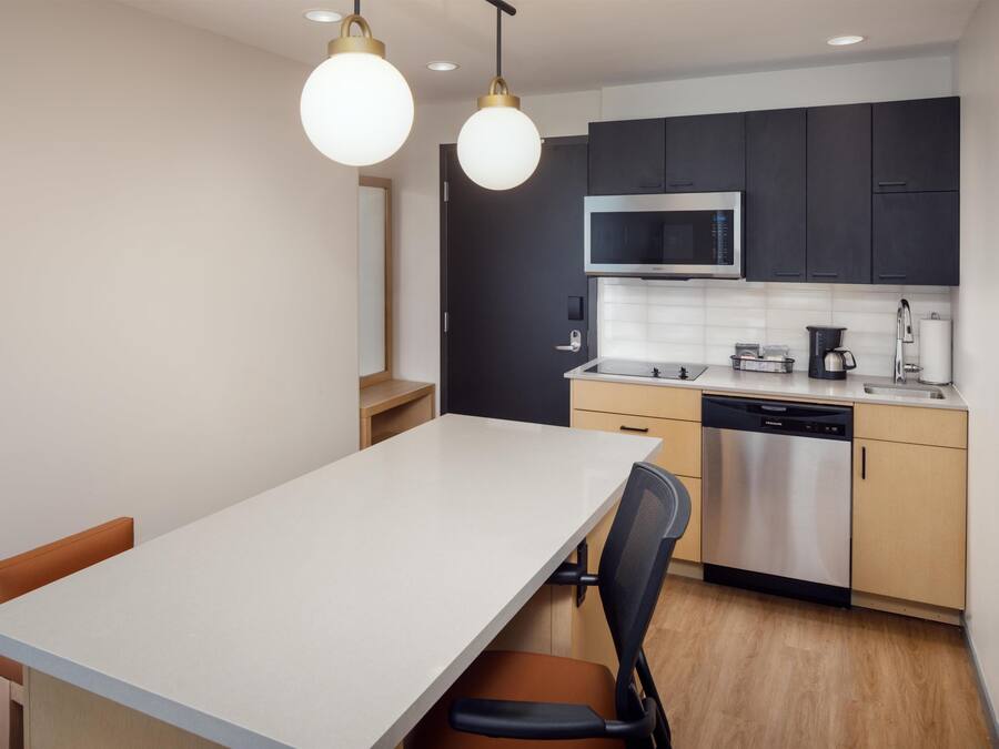 Une cuisine moderne dotée d’un plan de travail blanc, d’appareils électroménagers en acier inoxydable et d’un coin repas avec une table et des chaises.