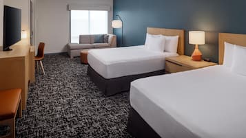 A hotel room with two beds, a desk, a chair, a sofa, and a television.