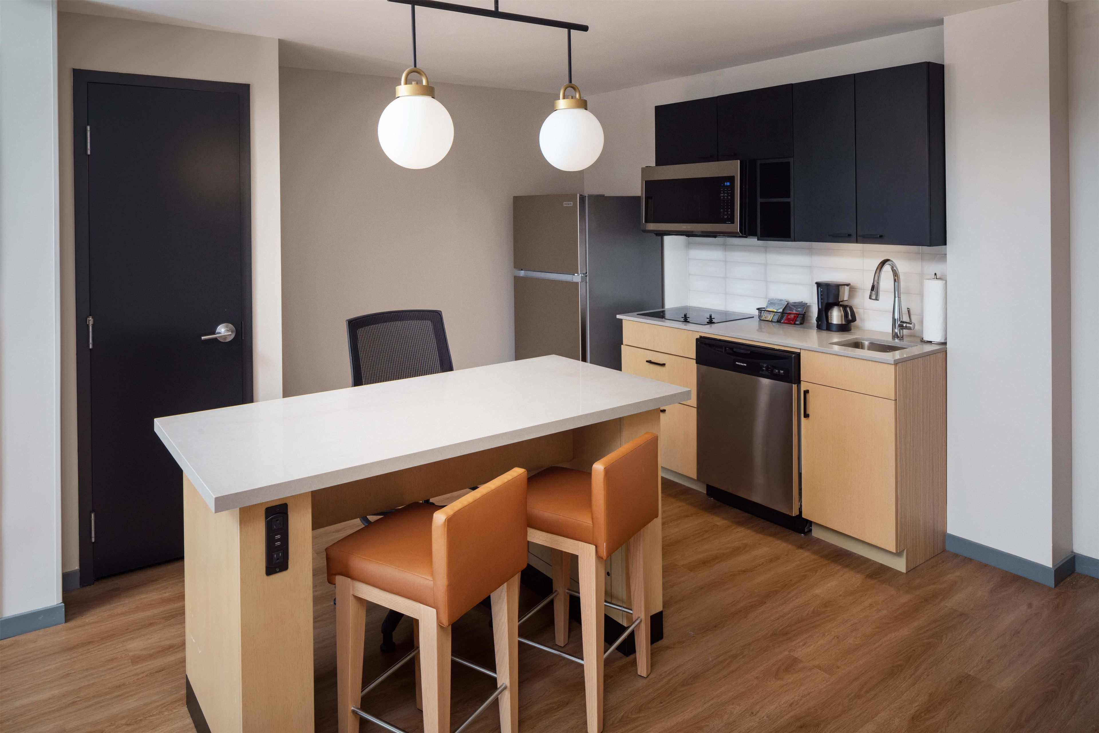 A modern kitchen with a central island, two bar stools, a microwave, a dishwasher, and a coffee maker.
