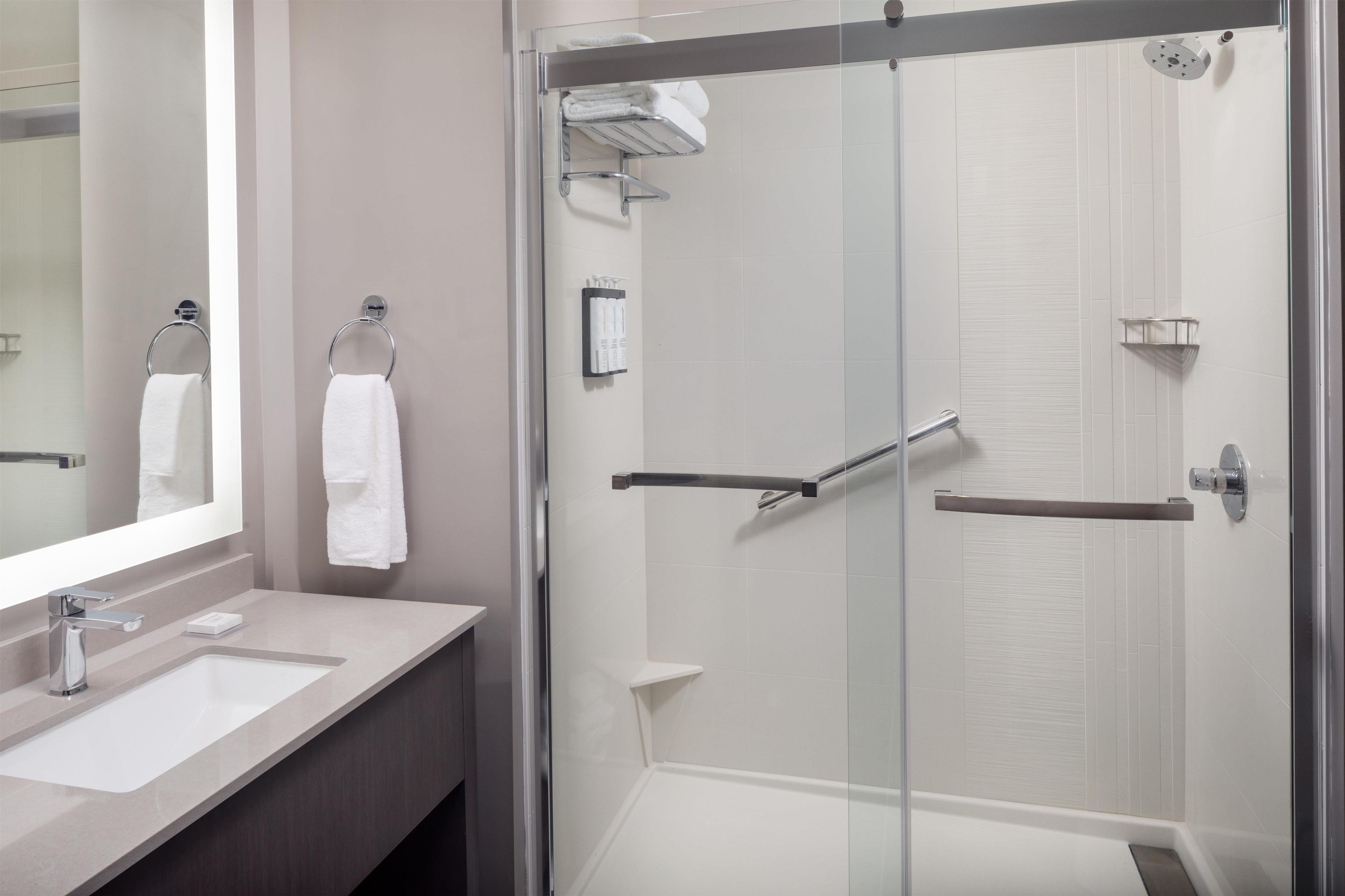 Een moderne badkamer met een douche met glazen wand, een wastafel met spiegel en twee handdoekhouders.