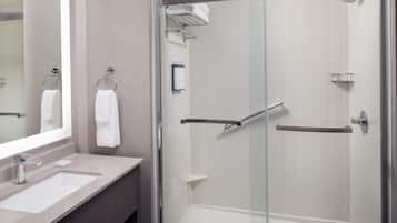 Un baño moderno con cabina de ducha acristalada, tocador con espejo y dos anillas para toallas.