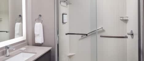 Un baño moderno con cabina de ducha acristalada, tocador con espejo y dos anillas para toallas.