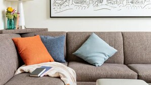 A grey sofa with three cushions in different colors, a white cushion, and a book on the left side. - Hyatt House Destin (Destin)