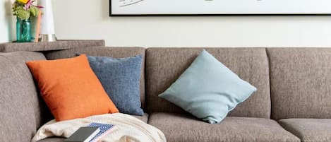 A grey sofa with three cushions in different colors, a white cushion, and a book on the left side.