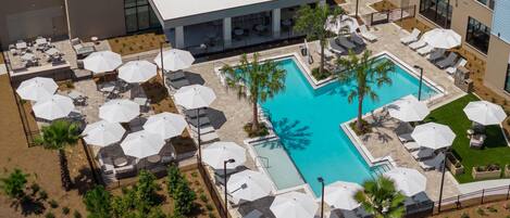 An aerial view of a hotel with a swimming pool, sun loungers, and umbrellas.