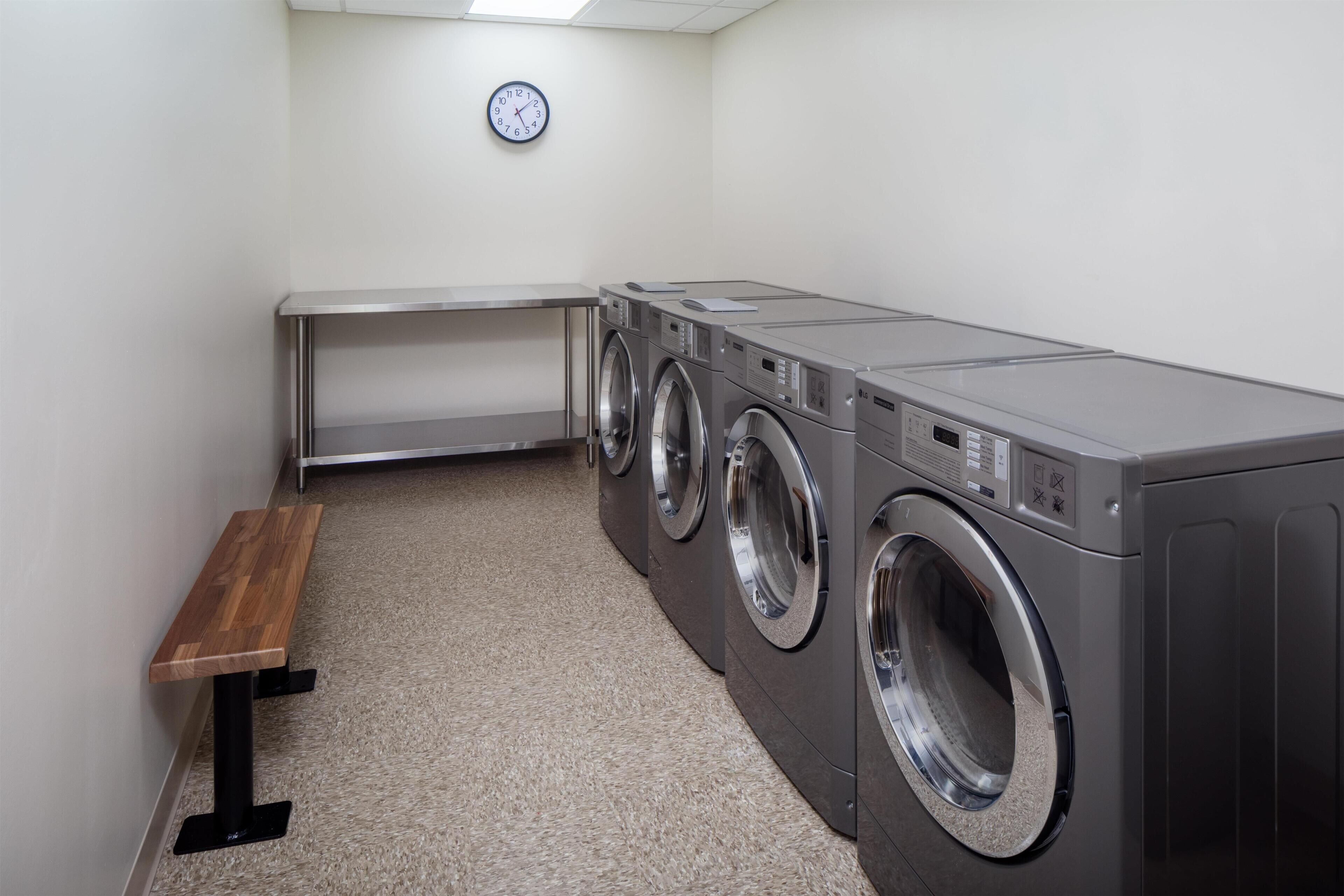A laundry room with a bench, three stacked washing machines, and a clock on the wall.