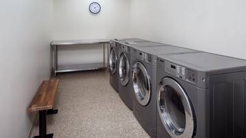 A laundry room with a bench, three stacked washing machines, and a clock on the wall.