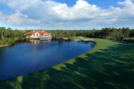 A golf course with a water body, a house with a red roof, and a forested area.