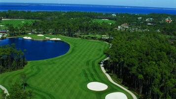 Un campo de golf con un lago grande, rodeado de árboles y un cielo azul despejado.