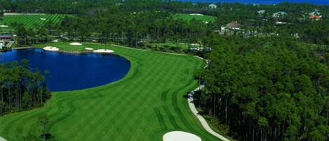 A golf course with a large lake, surrounded by trees and a clear blue sky.