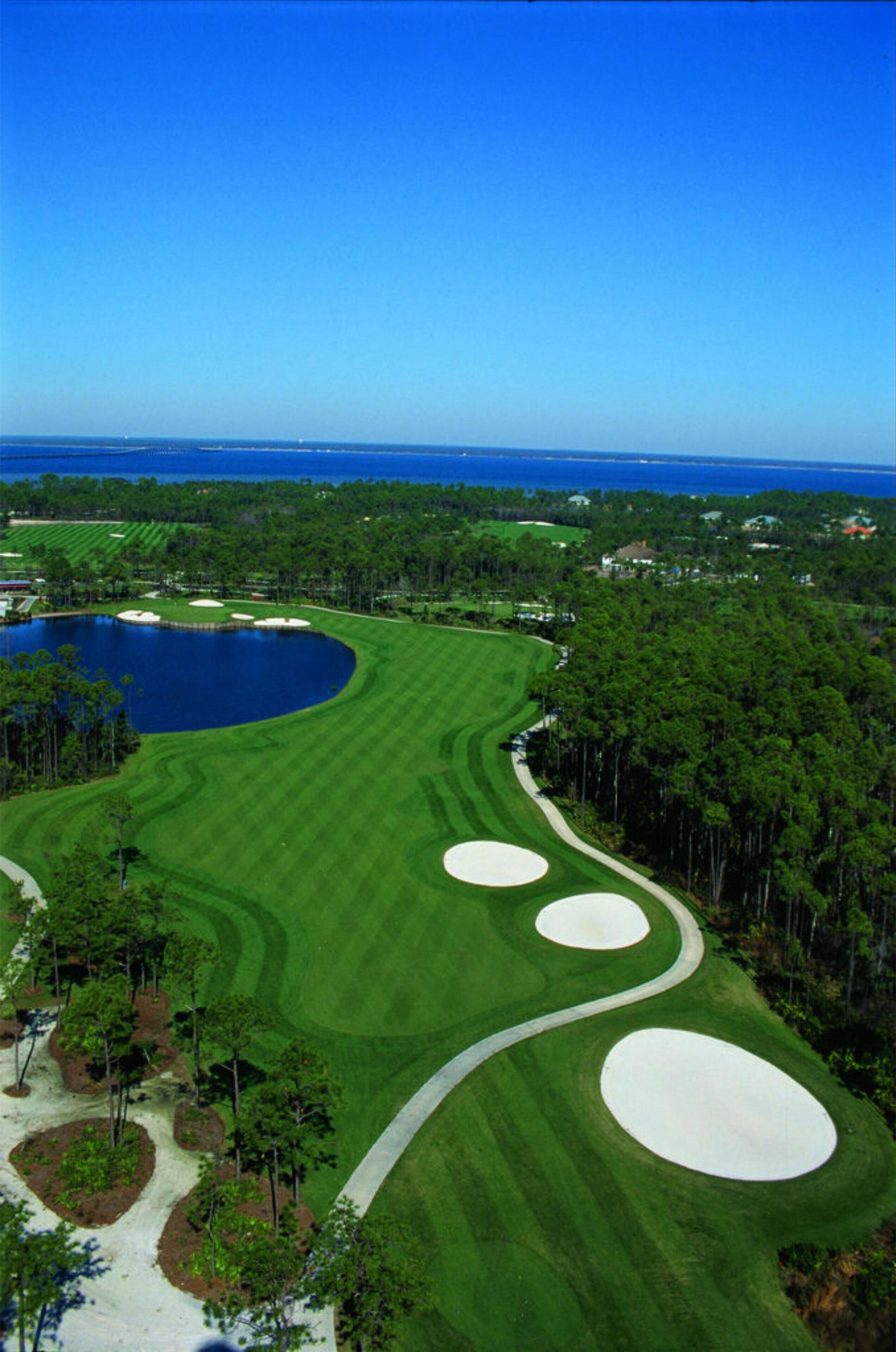 Un campo de golf con un lago grande, rodeado de árboles y un cielo azul despejado.