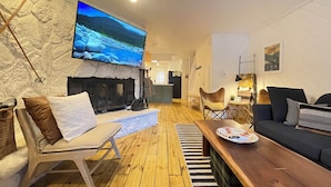 Ein gemütliches Wohnzimmer mit Steinwand, Kamin, Fernseher und Holzboden.