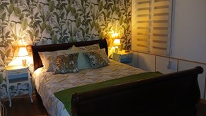 Une chambre à coucher avec un lit, deux tables de chevet, une commode et une fenêtre avec des stores.