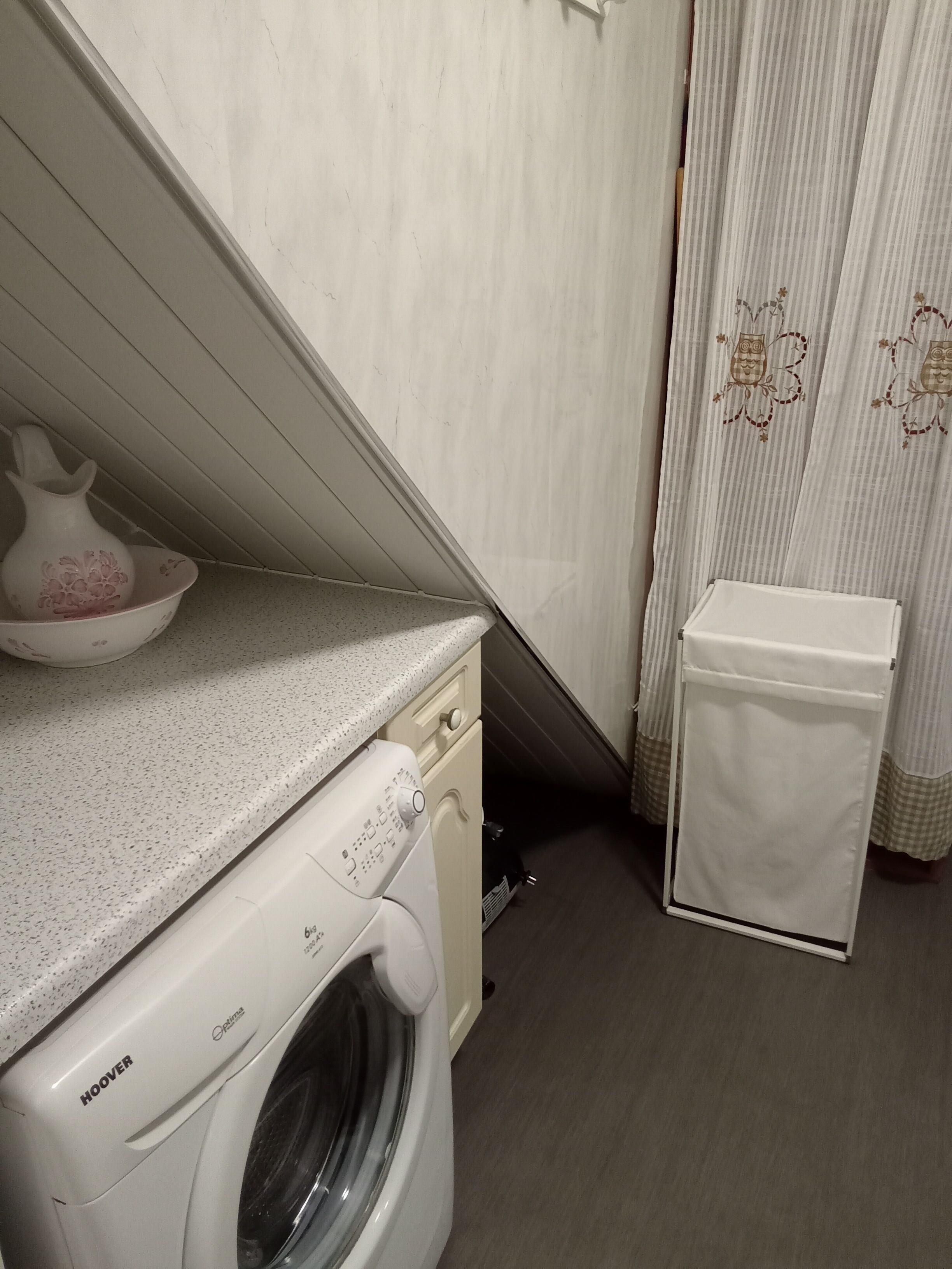 Un espace buanderie compact comprenant un lave-linge à chargement frontal, un petit meuble blanc et un étendoir mural.