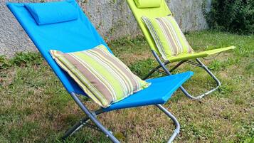 Deux chaises de jardin avec coussins, placées sur une pelouse verdoyante, avec un mur de pierres en arrière-plan.
