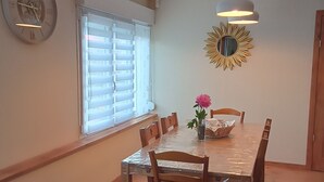 Un coin repas comprenant une table, des chaises, une horloge, une fenêtre avec des stores et un miroir en forme de soleil.