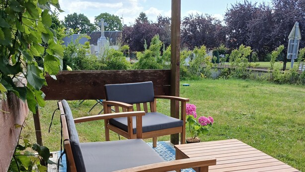 Une terrasse extérieure aménagée avec des meubles en bois, notamment un banc et une table, posés sur un tapis à motifs.