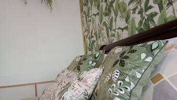 A bed with patterned pillows, a wall with a plant-themed wallpaper, and two hanging baskets.