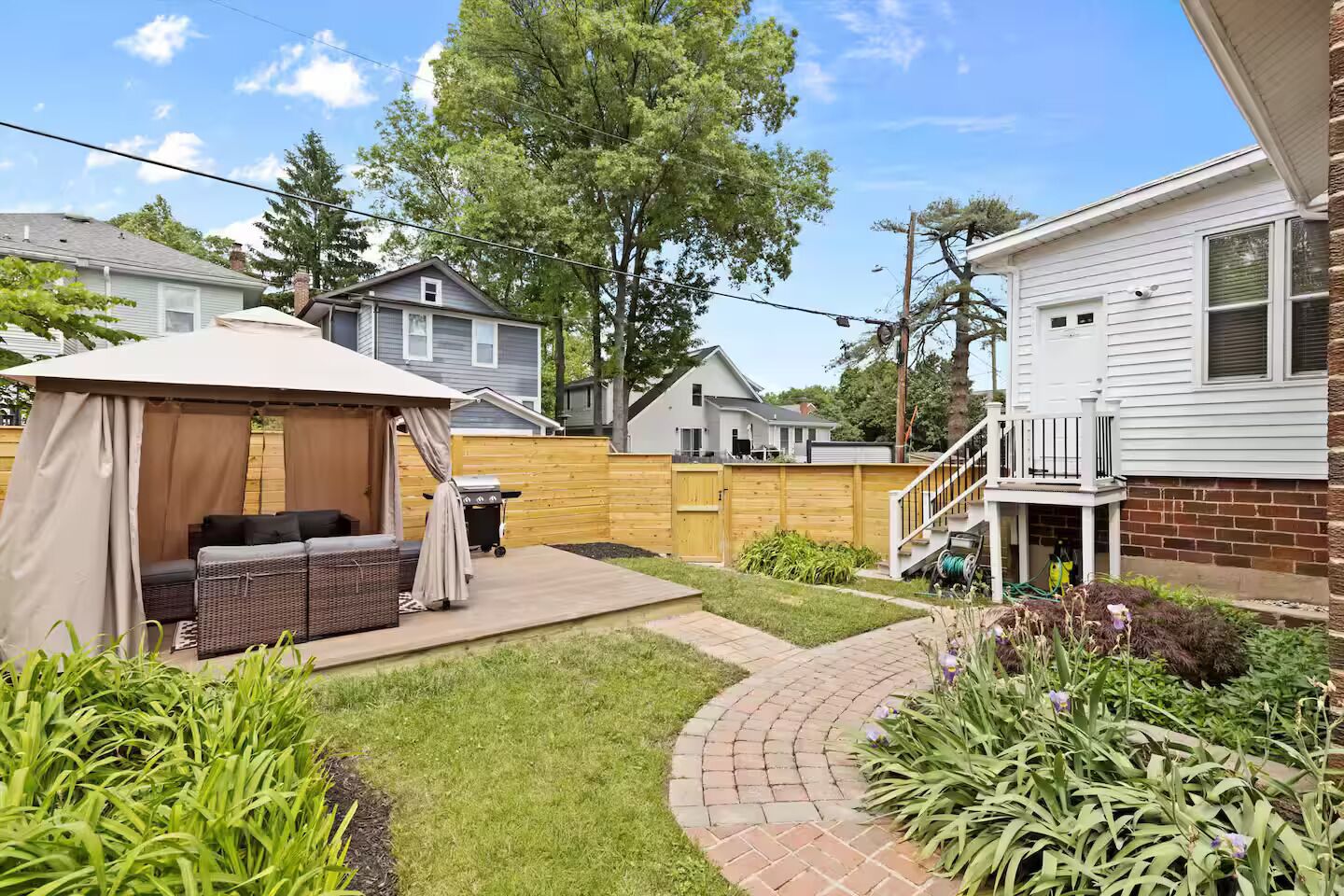 A backyard with a covered seating area, a grill, and a brick pathway.