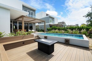 A modern outdoor pool area with a wooden deck, lounge chairs, and a pergola. - BRAND NEW Villa Between 2 Blues, Beachwalk Villa 5 (Providenciales)