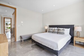 A modern bedroom with a large bed, bedside lamps, a bench, and a wooden nightstand. - BRAND NEW Villa Between 2 Blues, Beachwalk Villa 5 (Providenciales)