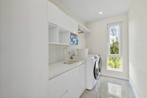 A modern kitchen with a built-in washer and dryer, a sink, and a window providing natural light. - BRAND NEW Villa Between 2 Blues, Beachwalk Villa 5 (Providenciales)
