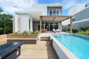 Ein moderner Poolbereich im Freien mit Holzterrasse, Liegestühlen und einer Pergola.