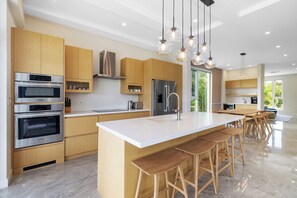 Eine moderne Küche mit Edelstahlgeräten, Holzschränken, einer großen Kochinsel mit Barhocker und Pendelleuchten.