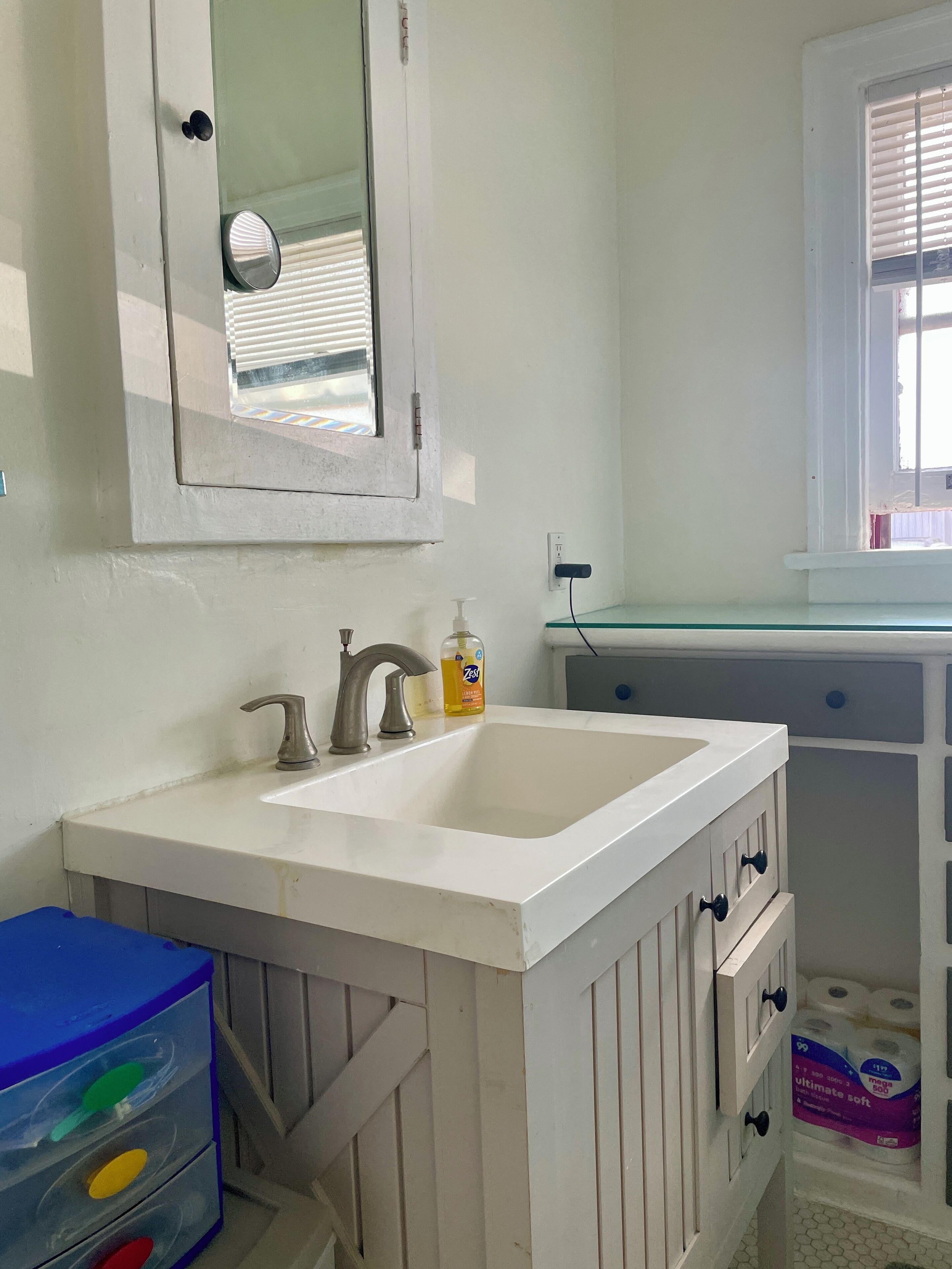A bathroom with a white sink, a mirror, and a window with blinds.