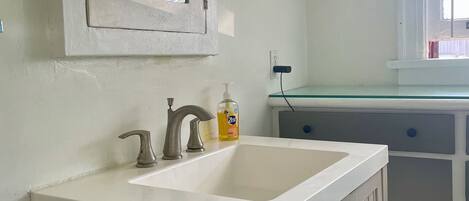 A bathroom with a white sink, a mirror, and a window with blinds.